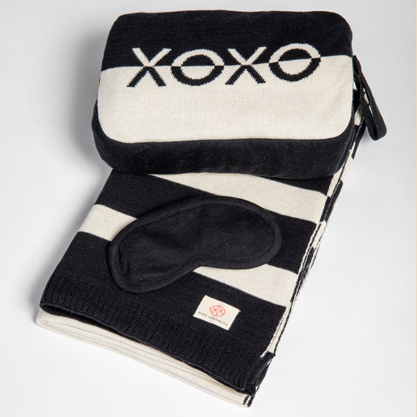 Black and white folded striped blanket with a sleep mask and pouch on a light gray background