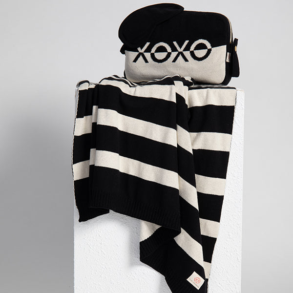Black and white striped blanket with a eye mask and pouch on a light gray background