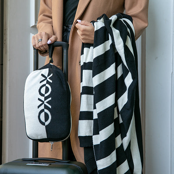 Person holding a black and white striped blanket and a black travel bag with a XOXO logo.