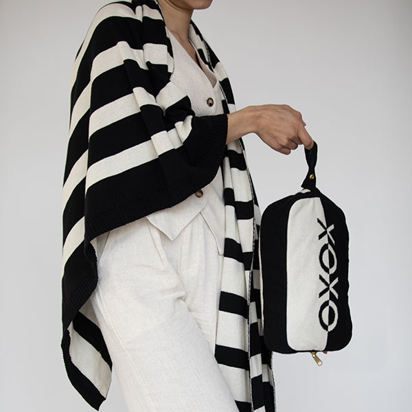 Person holding a black and white bag with 'XOXO' branding and wearing a matching cotton blanket against a plain background