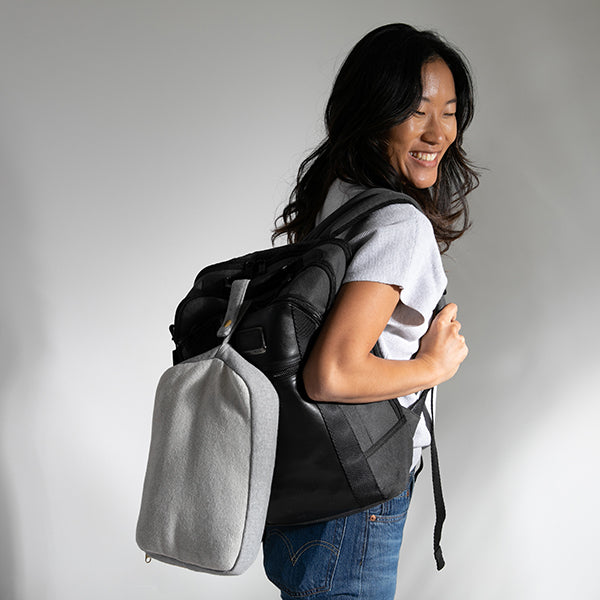Woman carrying a black and grey backpack with a travel blanket pouch against a plain background.