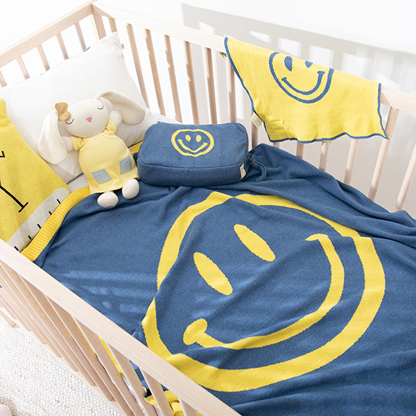 Baby crib with blue and yellow smiley face blanket, blanket pouch, and plush bunny toy.