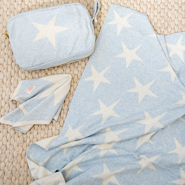 Sky blue baby blanket with star pattern, baby wipes, and a small bag on a textured knit mat.