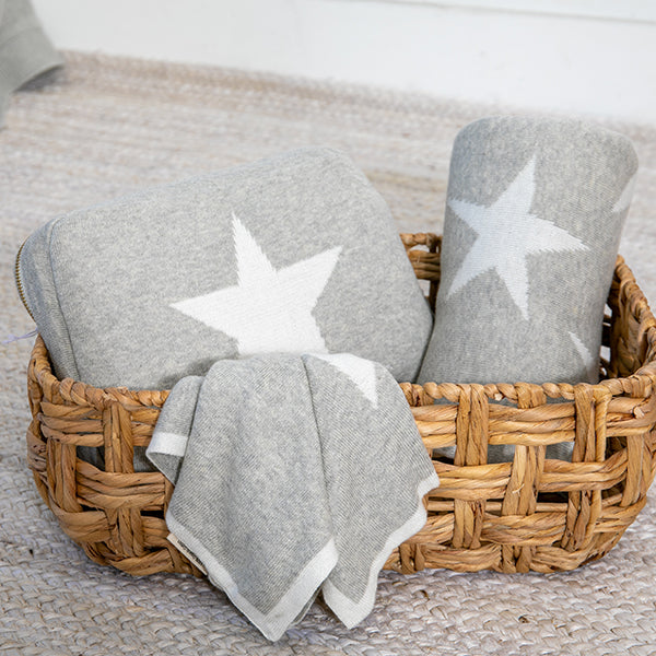 Vanilla and light gray baby blanket set with white star patterns in a woven basket on a textured mat.