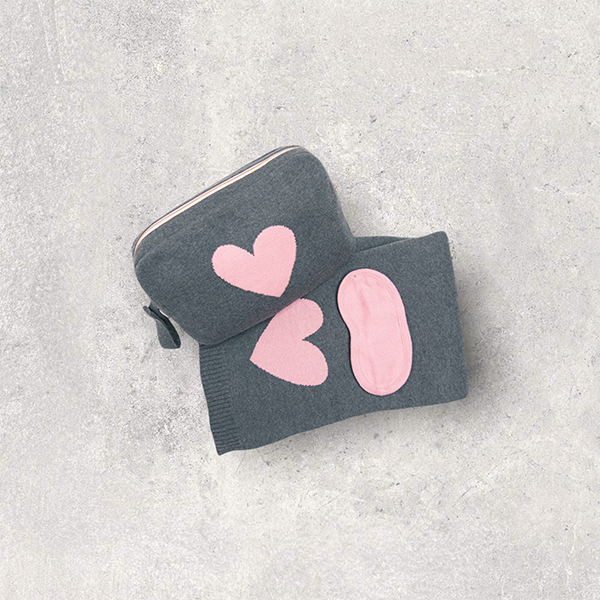 Grey organic cotton travel blanket and pink eye mask set with a grey and pink heart travel pouch for women, ready for airplane or road trip travel.