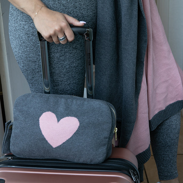 Traveler with carry-on bag and grey and pink reversible travel blanket bag with heart motif.