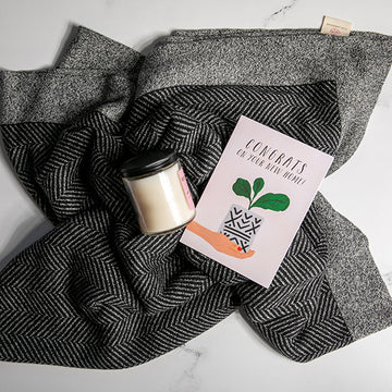 Black and white grindle organic cotton blanket with chevron texture knit under a candle and a card on a white surface.