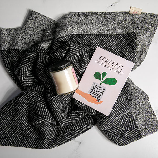 Black and white grindle organic cotton blanket with chevron texture knit under a candle and a card on a white surface.