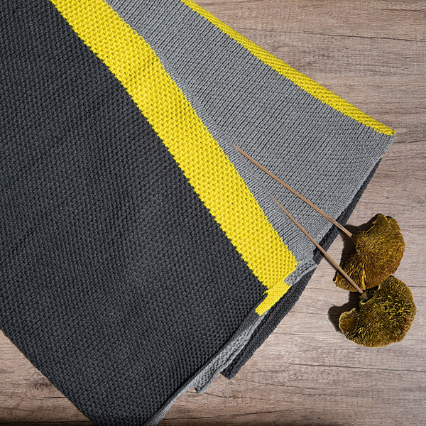 Gray and yellow woven organic cotton throw blanket with dried plants on a wooden surface.