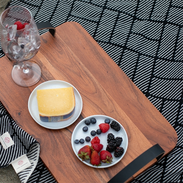 Cotton throw with black and white bricks and dashed designs under a wooden tray with cheese, berries, and a wine glass.