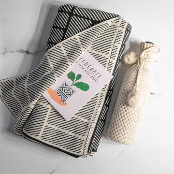 Organic cotton throw blanket with black bricks and dash pattern folded next to a knitted cotton beige wine sleeve. 