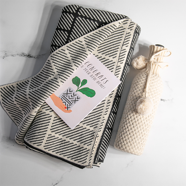 Organic cotton throw blanket with black bricks and dash pattern folded next to a knitted cotton beige wine sleeve. 