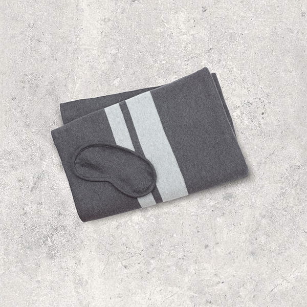 Gray eye mask and folded blanket with light grey stripes on a light gray textured surface.