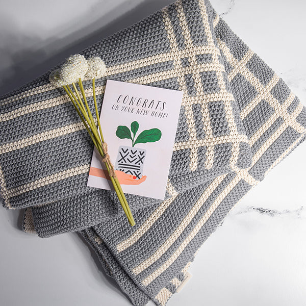 Light gray and white striped and textured cotton blanket with a card and flowers on a light gray background.