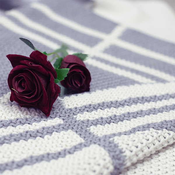 Two red roses placed on a striped double moss knit organic cotton light grey throw blanket.