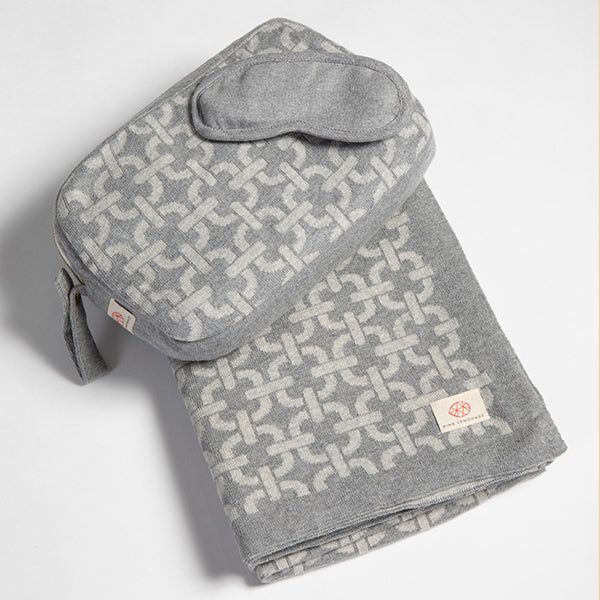 Gray link patterned cotton blanket with pouch and eye mask on a light gray background.