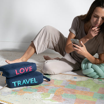 Woman sitting on a map with travel-themed blue travel pouches and a phone.