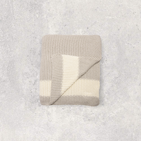 Folded beige and white moss knit cotton throw blanket on a textured gray surface.