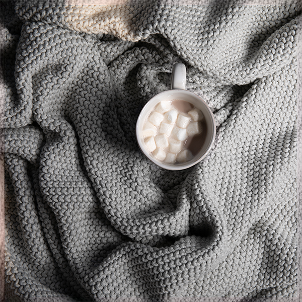 Cup of hot chocolate with marshmallows placed on a textured moss-knit stitched cotton blanket.