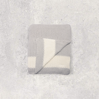 Gray and white moss knitted cotton blanket with a white strip folded on a textured gray surface.