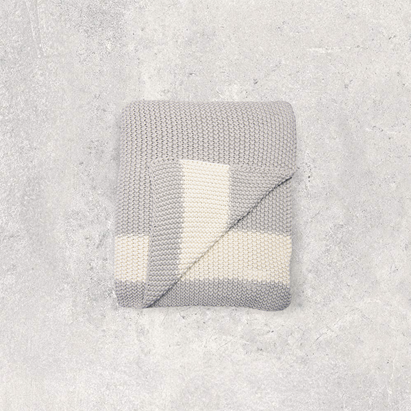 Gray and white moss knitted cotton blanket with a white strip folded on a textured gray surface.