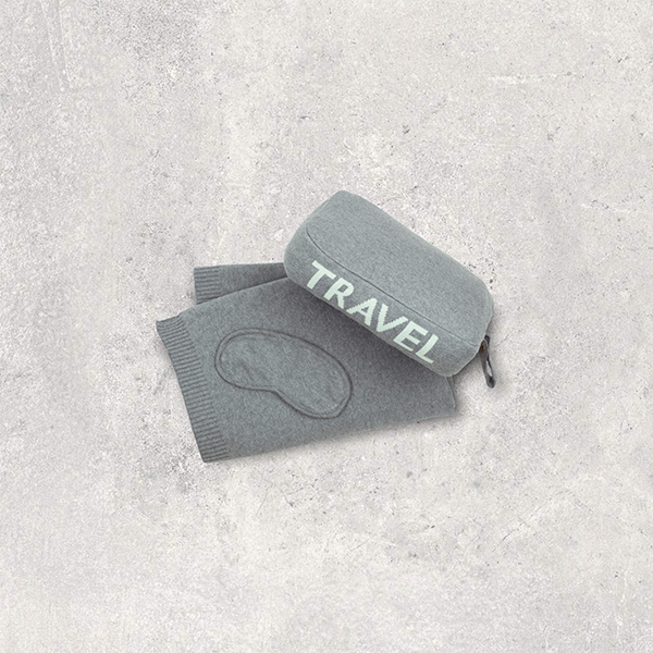 Gray travel set with words 'Travel' in mint green pouch and eye mask on a textured gray surface