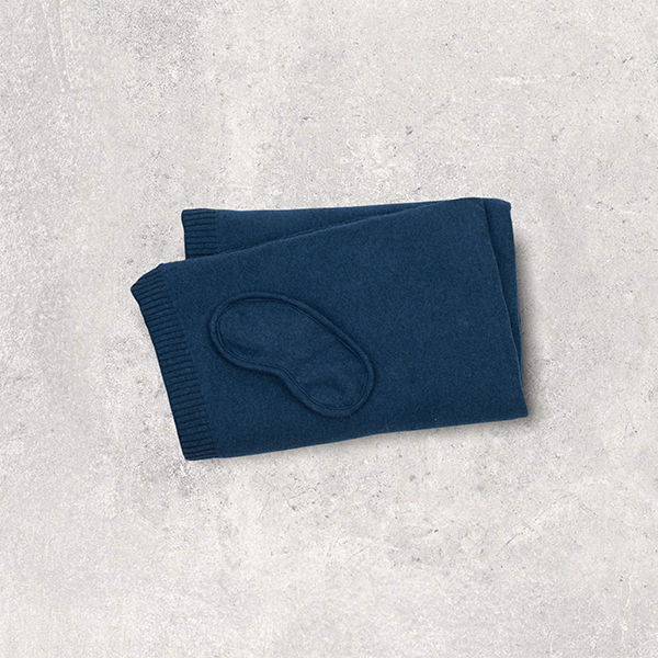 Folded navy blue organic cotton blanket with navy blue eye mask on a light gray textured surface