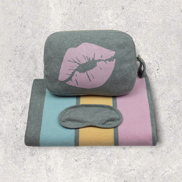Travel set with pouch with pink lips, eye mask, and striped blanket on a textured surface.