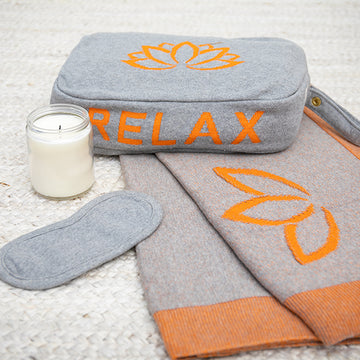 Gray and orange travel blanket set with 'RELAX' text and lotus design on a textured surface with a sleep mask and white candle.