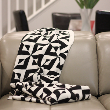 Black and white geometric patterned throw blanket draped over a beige sofa in a living room setting.