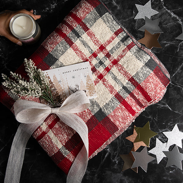 Red checked cotton throw with a candle, card, and decorative bow on a dark surface with star-shaped confetti.