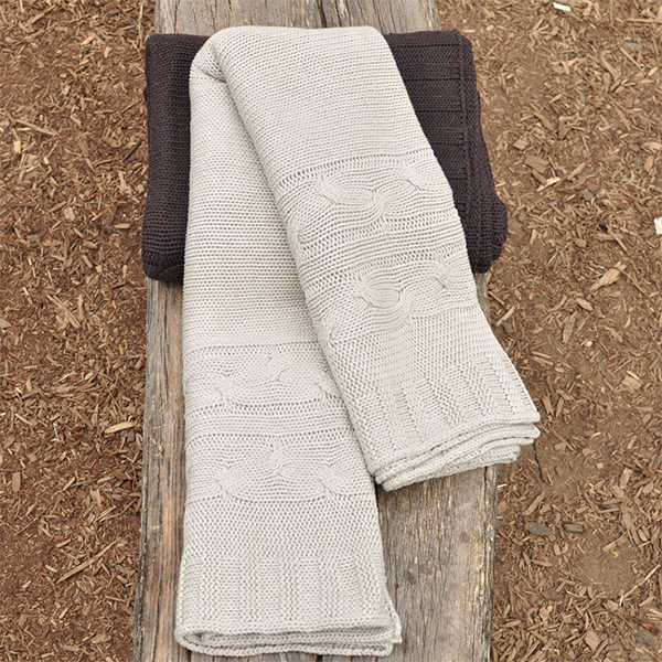 Folded beige cotton knit blanket placed on a wooden bench in the park while in the outdoors for a picnic.