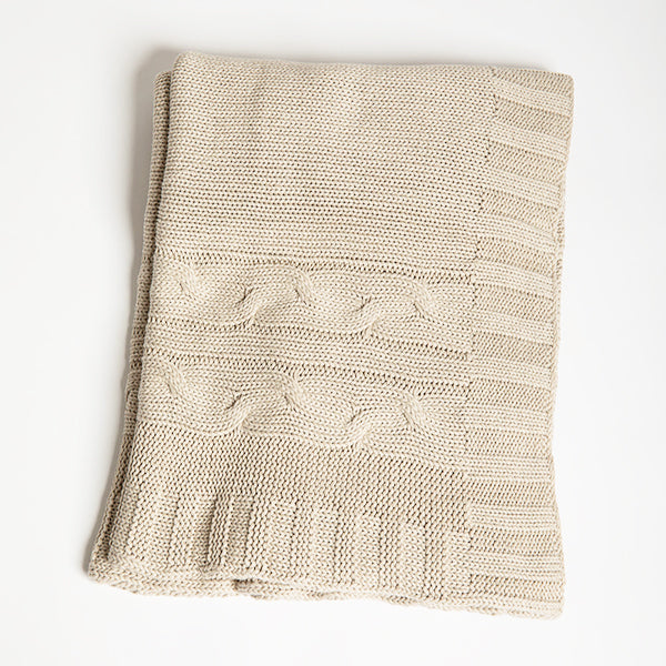 Beige knitted organic cotton blanket with cable patterns pictured on a white background.