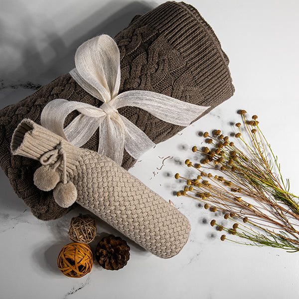 Chunky knitted dark brown blanket with a beige knitted wine sleeve and decorative elements on a light background.
