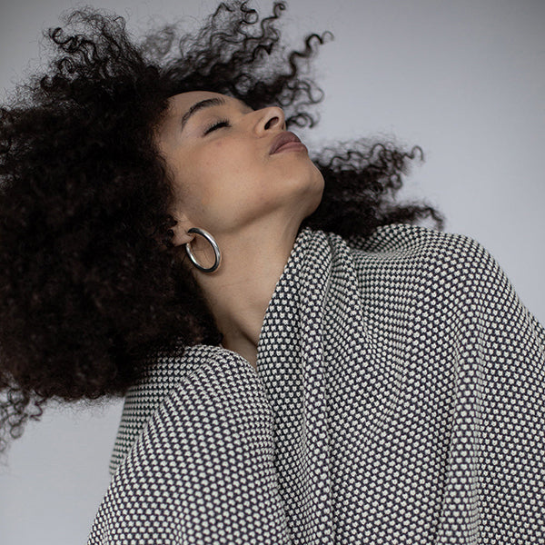 Woman with curly hair wrapped in a black and white patterned cotton blanket against a neutral background.