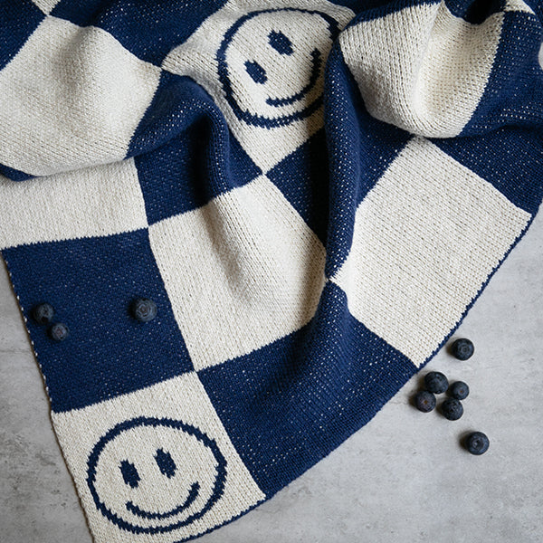 Close up of navy blue and white checkered throw blanket with smiley face patterns on a gray surface.