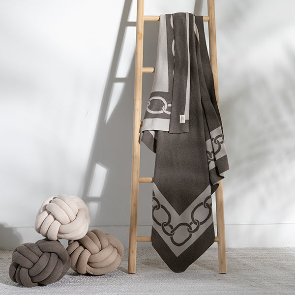 Decorative throw blanket with geometric chain pattern draped over a wooden ladder, next to knot pillows.