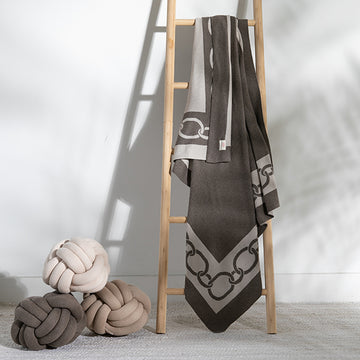 Decorative throw blanket with geometric chain pattern draped over a wooden ladder, next to knot pillows.