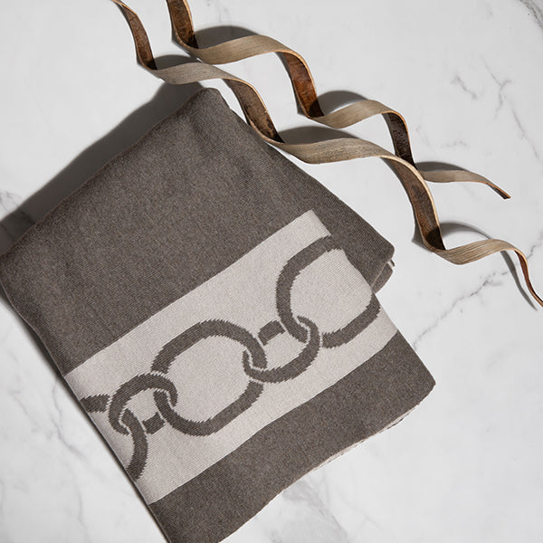 Dark brown blanket with chain pattern folded on a light background with decorative wooden bark.