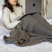 Person using a laptop on a bed and wrapped in a textured dark pewter throw blanket.
