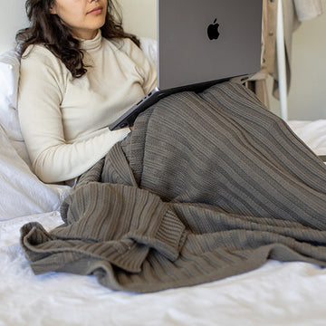 Person using a laptop on a bed and wrapped in a textured dark pewter throw blanket.
