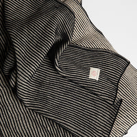 Close-up of a black and white striped throw with the Pink Lemonade brand label pictured a light gray background.