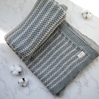 Light gray and white striped organic cotton knitted throw on a marble surface with cotton buds.