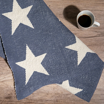 Star-patterned flintstone blue and white throw blanket on a wooden surface with a cup of coffee.