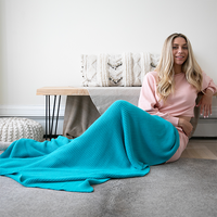 Woman sitting on a couch with a blue blanket draped over her, in a cozy living room setting.