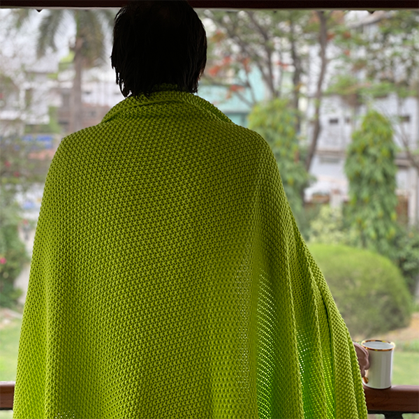Person wearing a neon yellow chunky knit throw looking out of a balcony with a garden view.