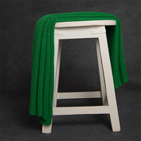 Chunky knitted scenic green organic cotton throw blanket draped over a white stool against a dark background.