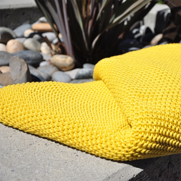 Yellow textured knitted cotton throw on a stone surface with succulent plants and pebbles in the background.