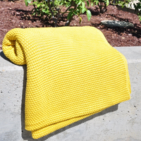 Bright yellow chunky knitted cotton throw on a concrete outdoor surface with plants in the background.