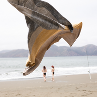 Textured yellow cotton blanket  with two people walking on a beach in the background.